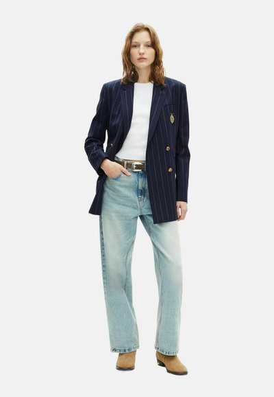 Blazer doppiopetto a righe navy con bottoni dorati, t-shirt bianca, jeans a gamba larga blu chiaro e stivaletti beige.