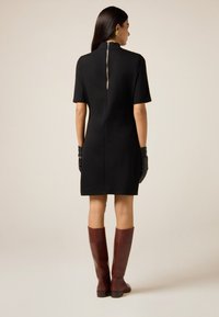 Czarna sukienka z krótkim rękawem, ze stójką i centralnym zamkiem z tyłu. W zestawie z brązowymi botkami sięgającymi do kolan i czarnymi rękawiczkami.