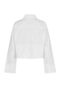 Veste blanche courte à manches longues, présentant des motifs brodés subtils, un col classique et des poignets boutonnés. Tissu en coton lisse.