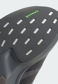 Czarna gumowa podeszwa obuwia z teksturowaną powierzchnią, z zielonym logo "Continental" i wieloma owalnymi wycięciami dla lepszej przyczepności i elastyczności.