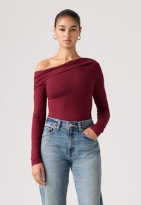 Μπορντό κορμάκι με μακριά μανίκια και ανοιχτούς ώμους, με λεπτομέρεια ρίγας, σε συνδυασμό με ανοιχτόχρωμα τζιν ψηλής μέσης. Λείο ύφασμα.