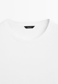 T-shirt blanc à col rond avec une étiquette de marque noire cousue à l'intérieur du col indiquant "Massimo Dutti Made in China."