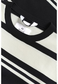 Pull tricoté avec des rayures diagonales noires et crème. Dispose d'un col rond et d'une étiquette portant la mention "Martinique" à l'intérieur du col.