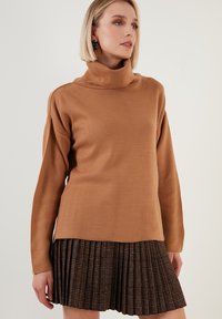Brauner Rollkragenpullover aus weichem Strickmaterial, kombiniert mit einem plissierten Rock mit einem mehrfarbigen Karomuster.