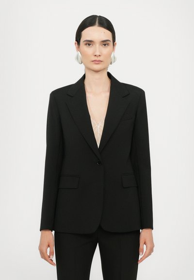 Black tailored blazer with notch lapels, single button closure, and two front pockets. Worn over a sheer top, featuring a smooth fabric texture.