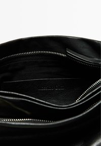 La borsa in pelle nera ha un interno con chiusura zip, fodera liscia e logo impresso. Superficie testurizzata con dettagli di cucitura sottili.