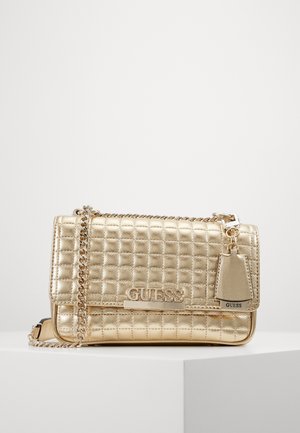 Goldene, gesteppte Leder-Umhängetasche mit Kettenriemen, GUESS-Logo-Plakette und passendem Lederanhänger auf weißer Oberfläche.