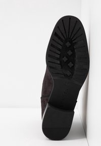 Semelle d'une chaussure noire vue de dessous, montrant le profil avec des motifs rectangulaires et en forme de trèfle, taille 37 embossée.
