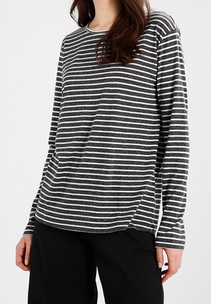 Person wearing a long-sleeve, dark gray shirt with white horizontal stripes and black pants against a plain background.