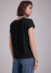 Black short-sleeve top with a relaxed fit, smooth texture, and a round neckline, paired with high-waisted light blue jeans.