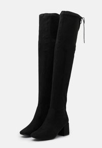 Botas de ante negras hasta la rodilla con tacón cuadrado, punta afilada y cierre ajustable en la parte superior. Textura suave y diseño ajustado.