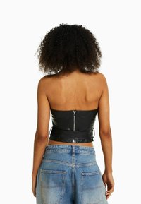 Top corto sin mangas de cuero negro con cremallera en la parte posterior, que presenta una silueta ajustada. Combinado con jeans de mezclilla de tiro alto en un tono azul claro.