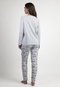 Una camiseta de manga larga gris clara combinada con pantalones de pijama de estampado que presentan personajes de dibujos animados en múltiples colores, hechos de tela suave.