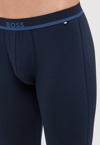 Marinblå tights med mjuk textur, som har en kontrasterande elastisk midja med "BOSS"-logotyp och en liten dekorativ detalj.