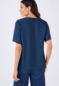 Maglietta blu scuro a maniche corte con una texture morbida e liscia e scollatura quadrata, abbinata a pantaloni in denim blu scuro.