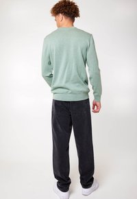Maglione verde con collo rotondo, maniche lunghe e polsini a coste abbinato a jeans in denim neri e sneaker bianche. Tessuto morbido, vestibilità casual.