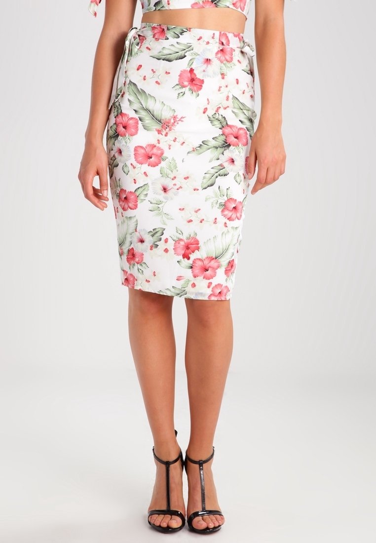 Femme portant une jupe crayon blanche avec un imprimé floral rose et des feuilles vertes, associée à des sandales à talons hauts noires à bride en T.