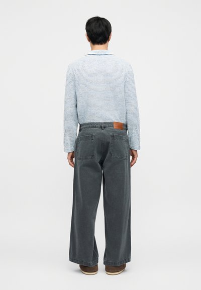 Μπλε και λευκή ριγέ μπλούζα με μακριά μανίκια και άνετη γραμμή, συνδυασμένη με σκούρο γκρι παντελόνι φαρδιάς γραμμής που διαθέτει δύο πίσω τσέπες και δερμάτινη ετικέτα.