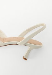 Bežid slingback sandaal õhukese rihmaga ja ruudukujulise bežihelega. Tekstureeritud sisetald sisaldab diskreetset brändimist, pakkudes luksuslikku disaini.