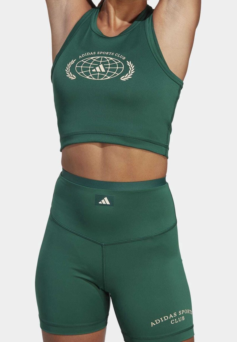 Top corto atletico verde e pantaloni corti a vita alta coordinati, realizzati in tessuto elasticizzato. Presenta un logo e cuciture decorative.