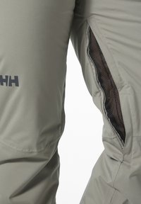 Pantalones exteriores ligeros y grises, fabricados con material impermeable, que cuentan con bolsillos laterales con cremallera y inserts de malla, además de una marca visible.