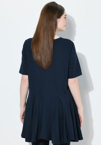 Túnica azul marino de manga corta con un diseño acampanado y detalles plisados en la parte posterior, hecha de una tela suave, adecuada para un uso informal.