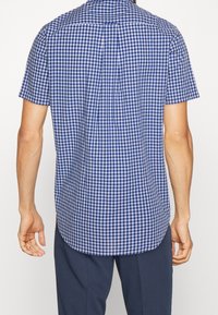 Camicetta a maniche corte, a quadretti blu e bianchi, realizzata in tessuto leggero; presenta un colletto button-down e un orlo curvo.