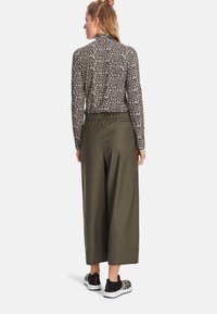 Leopard print top with a high neck, paired with olive green wide-leg pants and black slip-on shoes with a patterned accent.