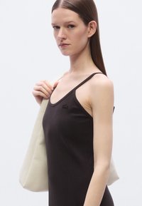 Débardeur marron côtelé à fines bretelles, avec un petit détail logo, associé à un sac cabas en cuir couleur crème.