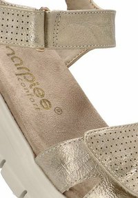 Sandalía metálica dorada con parte superior perforada, plantilla de textura suave, detalle de correa ajustable y suela blanca acolchada para mayor comodidad.