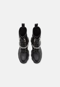 Svarta läderankelstövlar med en kraftig sula, snörning framtill och en silverkedjepynt. Slät textur och förstärkt häl.