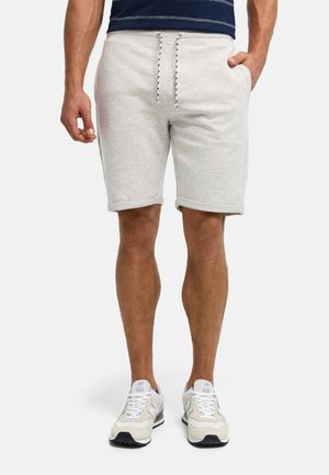 Mand iført lysegrå snøre shorts, hvide sneakers og en navyblå stribet skjorte med afslappede hænder ned langs siderne.