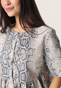 Robe légère à imprimé serpent en beige et noir, avec un col rond, des manches courtes et une jupe à volants froncée avec des détails de boutons.