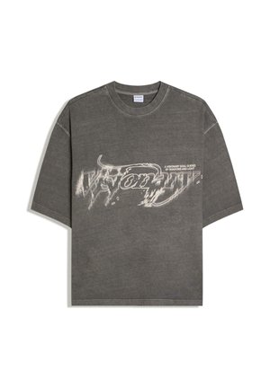 Ciemnoszary oversize T-shirt z zniekształconym białym napisem "Visionary" i mniejszym tekstem "A visionary soul guided by shadows and light" na przodzie.