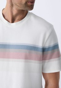 T-shirt blanc à col rond avec des rayures horizontales en bleu clair, rose et gris. Texture douce, coupe décontractée et manches courtes.