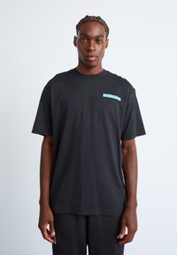 Sort kortærmet t-shirt i bomuld med et lysblåt grafisk motiv på venstre bryst. Lige pasform, rund hals, glat tekstur, minimalistisk design.