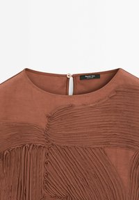 Blouse marron avec plis texturés et encolure ronde. Ouverture au dos avec un bouton. Étiquette : Massimo Dutti.