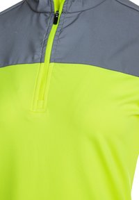 Lys gul pullover med en grå øverste del, der har en halv zip-lukning og en glat, let stofstruktur.