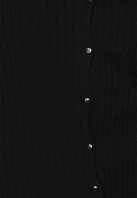 Černý žebrovaný kardigan z měkké látky, s přiléhavým střihem a kulatými černými knoflíky po celé přední části. Charakteristické detailní švy ve vlnitém vzoru.