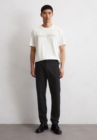 Weißes Baumwoll-T-Shirt mit "Marc O'Polo"-Logo, kombiniert mit schwarzen Anzughosen und schwarzen Schnürschuhen. Einfaches Design und entspannte Passform.