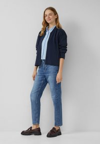 Marine bomberjack, gestreepte overhemd met knopen, blauwe spijkerbroek en donkere instappers. Casual outfit met een comfortabele pasvorm en effen kleuraccenten.