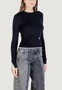Pull noir à côtes avec des manches longues, design ajusté et longueur courte, associé à un jean en denim gris taille haute avec une texture délavée.