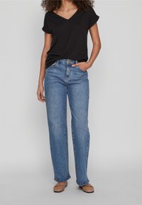 Černé tričko s výstřihem do V, modré vysoko pasové rovné džíny, béžové baleríny. Měkká tkanina, ležérní střih, žádné viditelné vzory nebo akcenty.