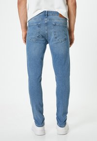 Jeans de denim azul con ajuste slim, diseño de cinco bolsillos y parche de cuero en la parte trasera de la cintura. Detalles de costura simples en toda la prenda.