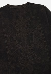 Zwarte oversized t-shirt met een textuurdesign op de rug, die een embleem met sierlijke details en wervelende patronen afbeeldt.