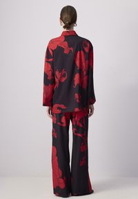 Zwei-teiliger Outfit bestehend aus einem schwarzen Stoff mit auffälligen roten Blumenmustern. Das Oberteil hat lange Ärmel und einen Kragen, kombiniert mit einer Hose mit weitem Bein.