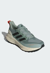 Zelená a šedá športová obuv s vodoodpudivým zvrškom, s čiernymi pruhmi, textúrovanou sieťovinou, oranžovým pätkovým popruhom a bodkovanou podrážkou.