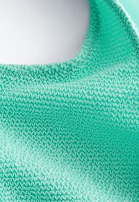 Gros plan sur un tissu turquoise avec un motif texturé, ondulé et froncé, et un bord d'encolure froncé.