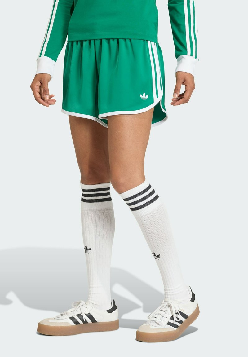Green athletic shorts with white trim, worn with white knee-high socks featuring black stripes and white sneakers with black accents.