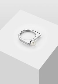 Anello in metallo argento con un design a punta e un accento di perla. Texture liscia, banda circolare e forma geometrica moderna.